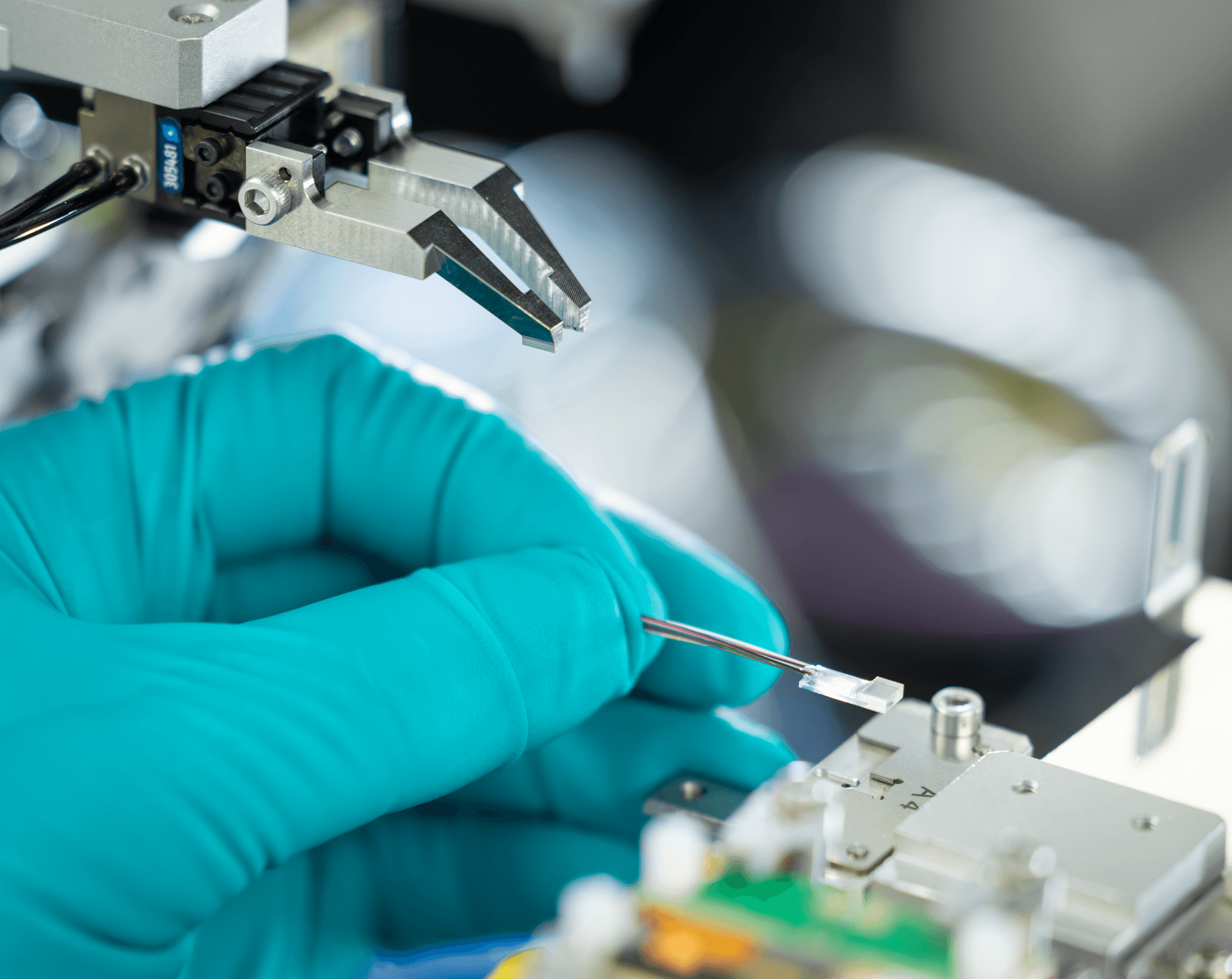 Gloved hand placing a fiber-coupled chip next to a precision gripper